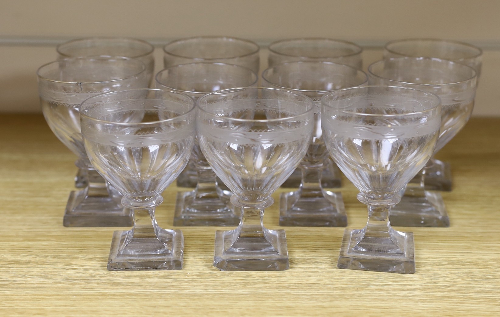 A set of eleven early 19th century engraved wine glasses, square foot, 11cm tall